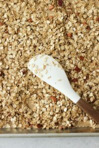 Spreading the granola evenly onto a cookie sheet with a spatula.