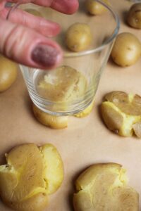 Using a small glass cup to press down on the cooked potatoes to smash them. 