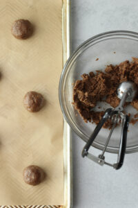 Placing the balls of dough onto a lined cookie sheet.