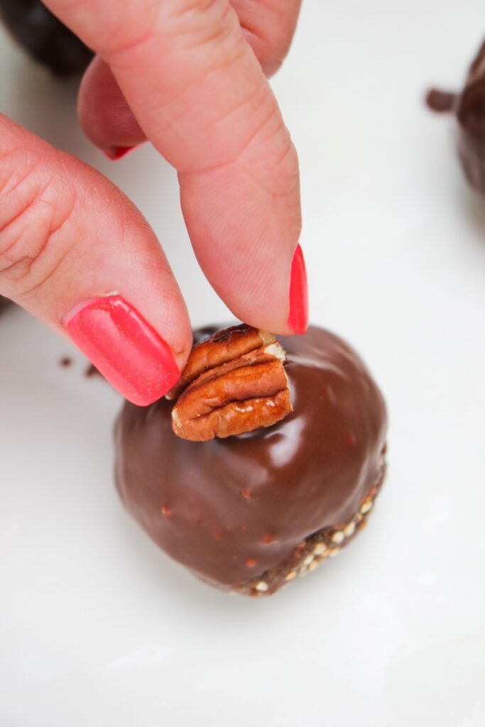 Placing a pecan piece on top of the wet chocolate topping.