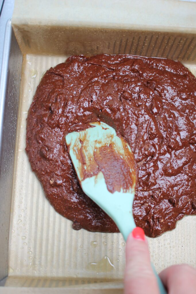 Spreading the batter into an even layer in the greased and lined pan.