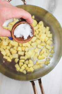 Adding the coconut oil to the pan of cubed apples.