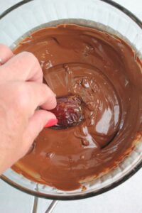 Dipping a stuffed date into the melted chocolate.