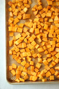 The butternut squash cubes are seasoned on a baking sheet and are ready to go in the oven.