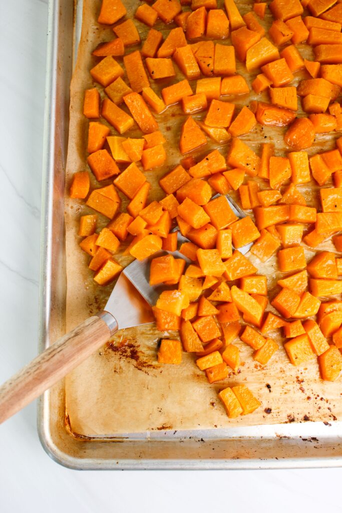 The roasted butternut squash cubes are hot out of the oven on a cookie sheet.