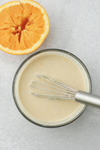 The orange tahini dressing has been whisked in a small glass bowl.