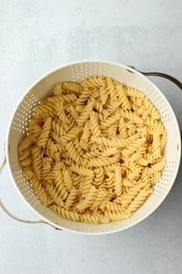THe noodles have been cooked and are in a white collander to drain.