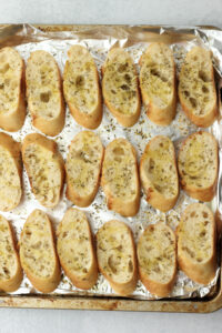 The baguette slices have been toasted on a tin foil-lined baking sheet.