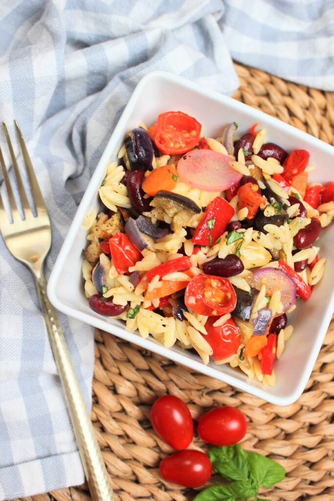 A bowl of vegan summer pasta salad with roasted veggies and orzo.