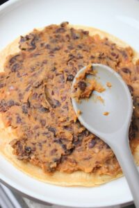 Spreading the bean mixture over the top of one corn tortilla.