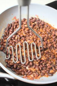 A potato masher is mashing up the black bean mixture.