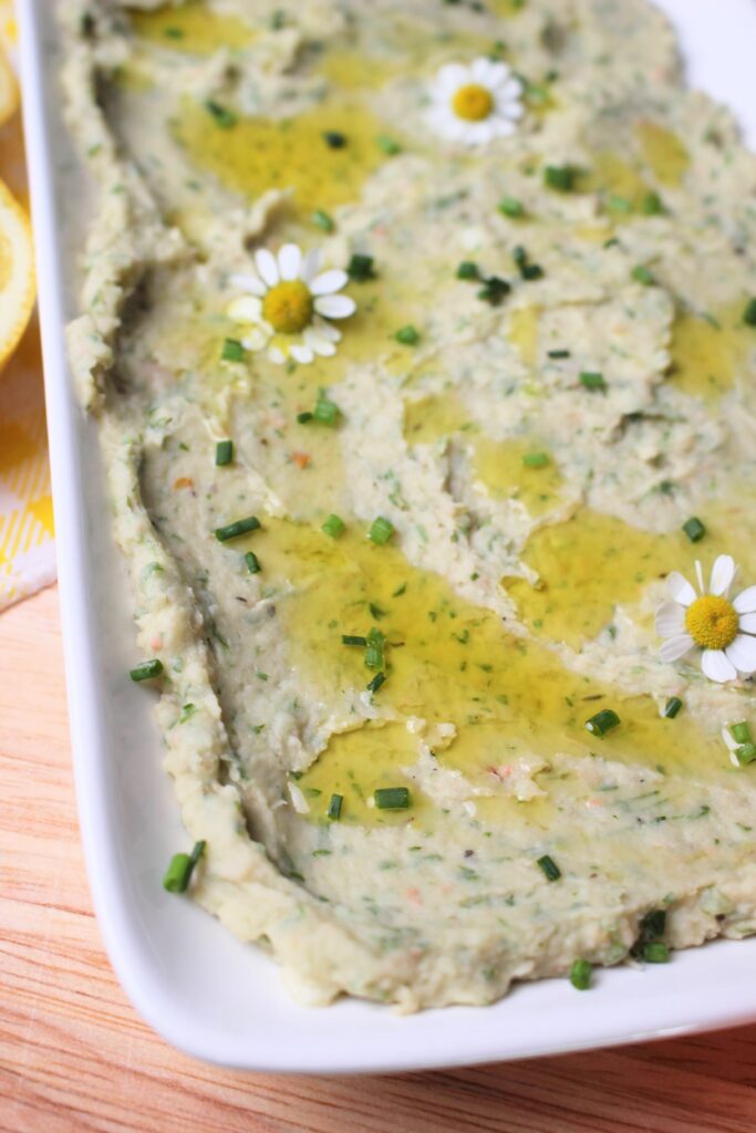 Up close picture of the plated white bean dip topped with an olive oil drizzle and minced chives. 