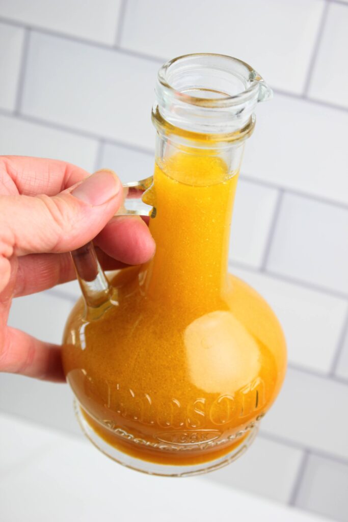Holding and ready to pour the pumpkin maple vinaigrette in a glass jar.
