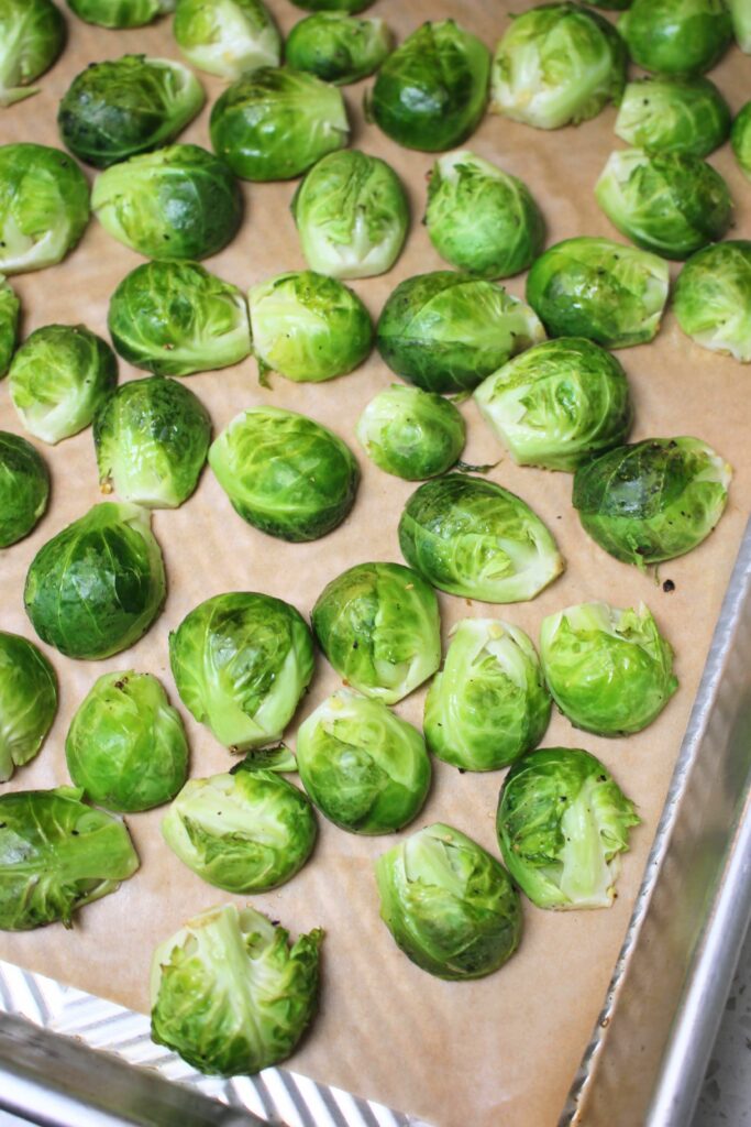 The halved brussels sprouts are laid cut side down on a lined cookie sheet.