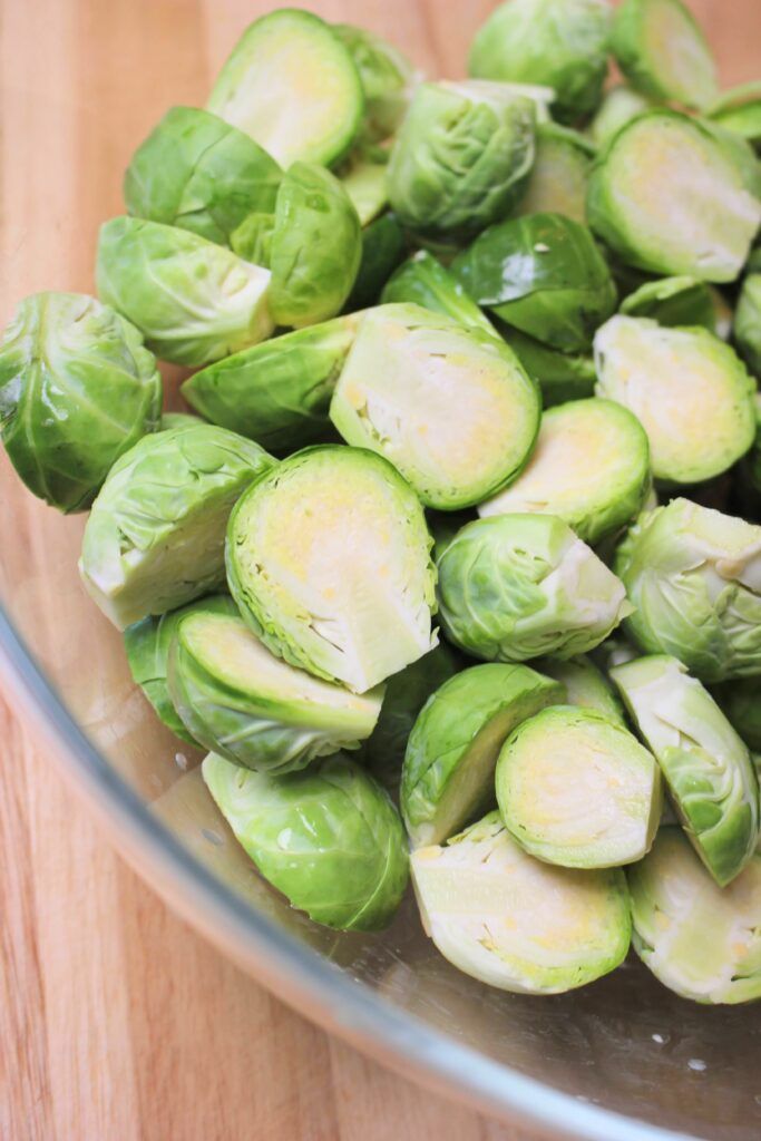 The brussels sprouts are cut lengthwise and put into a large glass bowl.