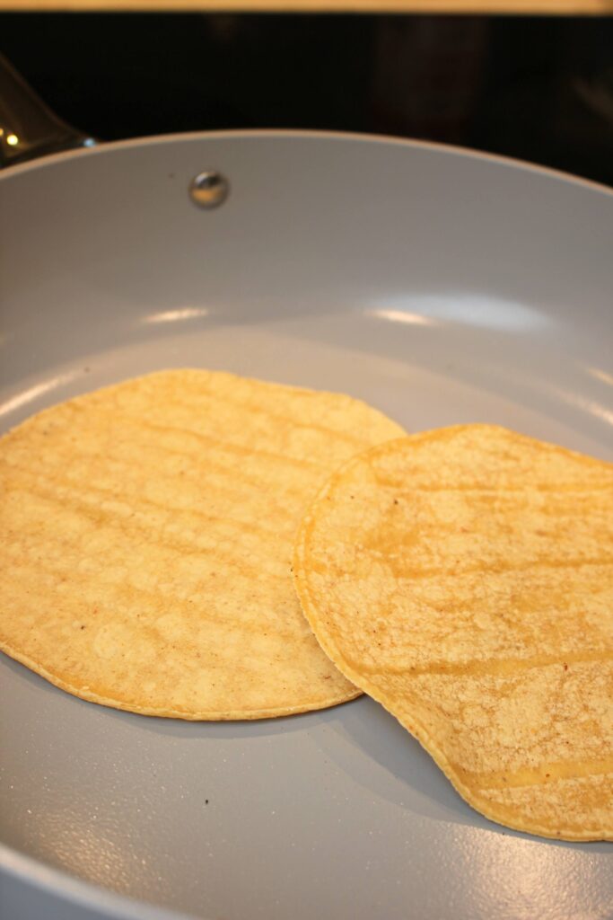 Warming up two corn tortillas in a frying pan.