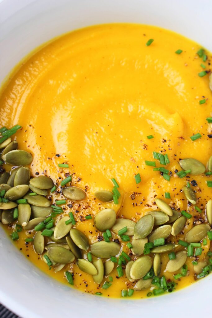 Vegan pumpkin soup topped with pumpkin seeds, chives, and pepper.