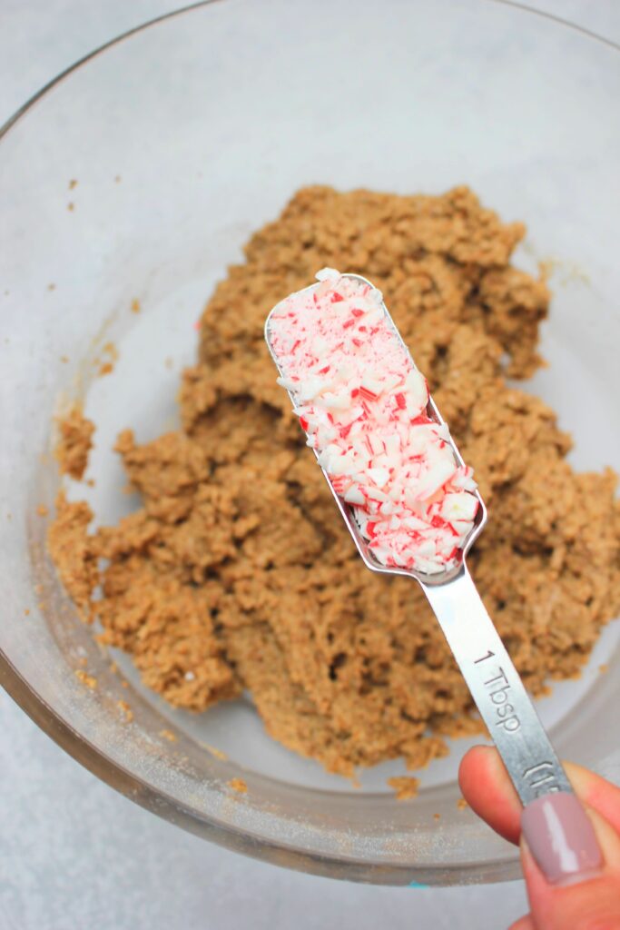 Pouring the crushed candy cane pieces into the bowl of dough.