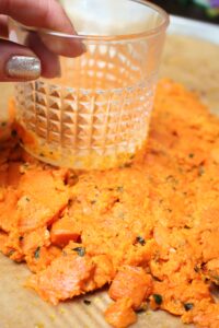 Using a glass cup to smash the sweet potatoes in the pan.