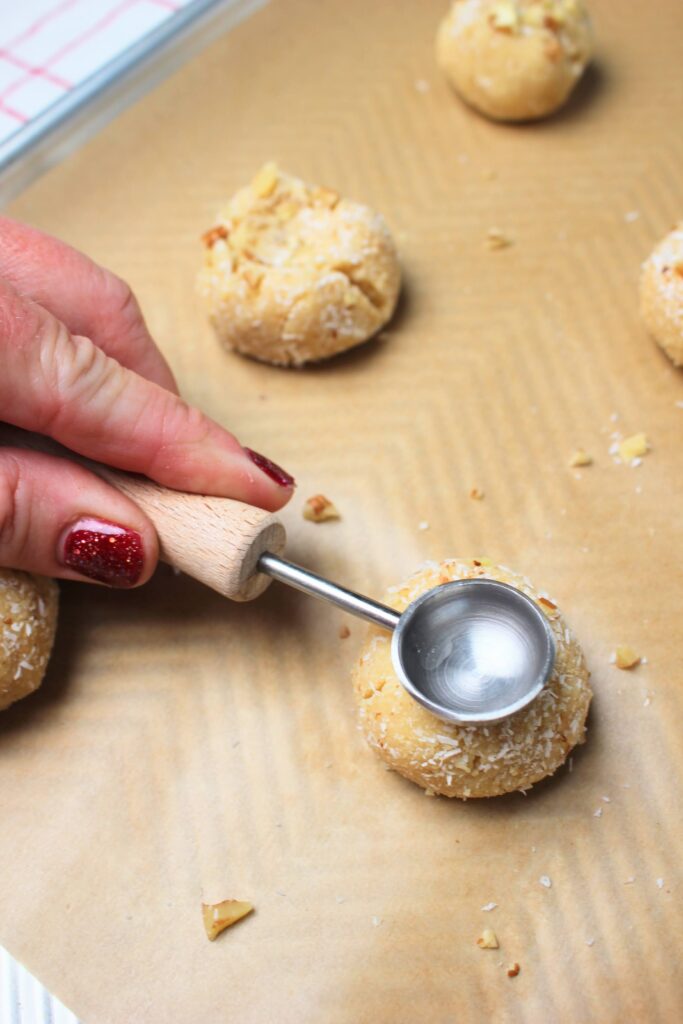 Pressing an indent into the top of a cookie dough ball with the back of a teaspoon.