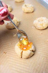 Spooning jam into the middle of a cookie.