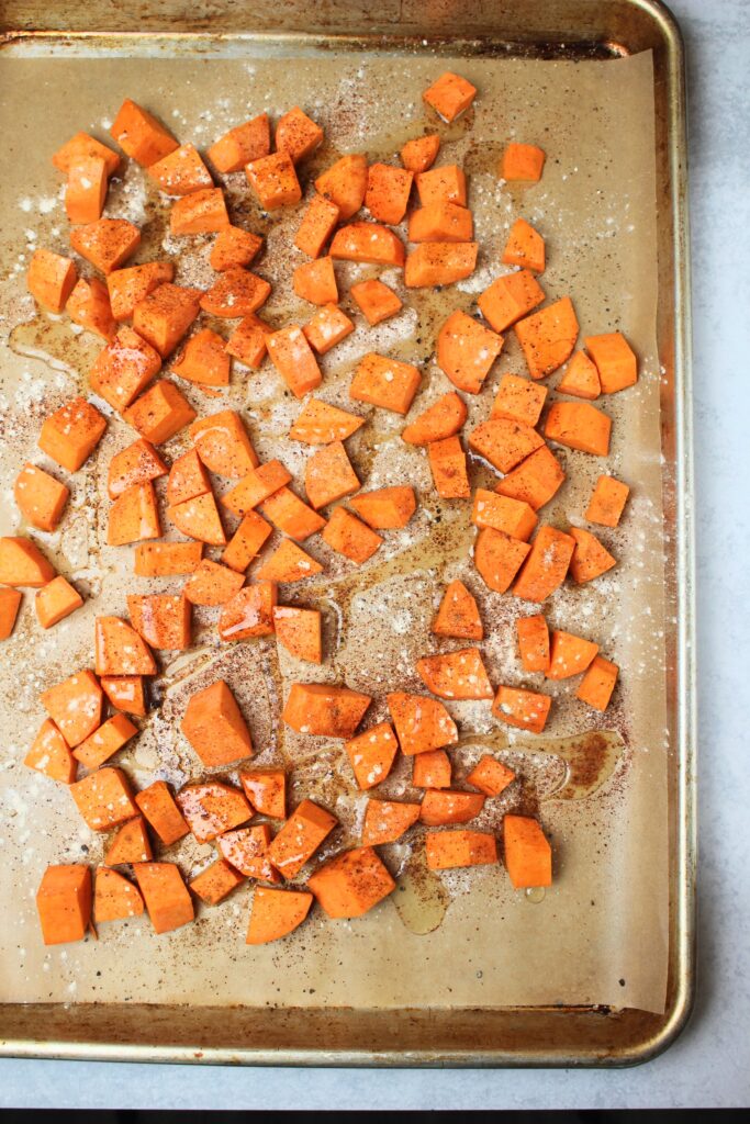 The sweet potato chunks are seasoned on a baking tray and ready to go in the oven.
