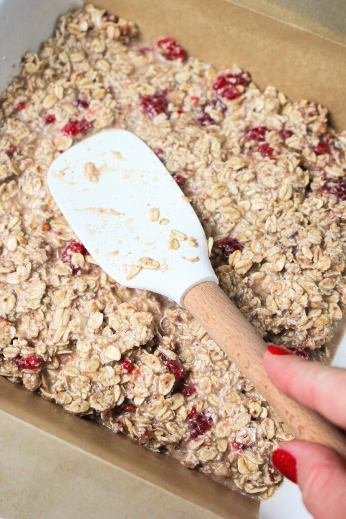 Spreading the wet oatmeal mixture into the casserole dish with a spatula.