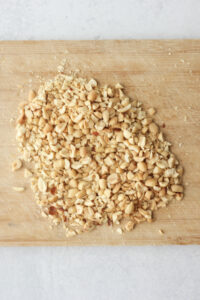 The chopped peanuts on a small wooden cutting board.
