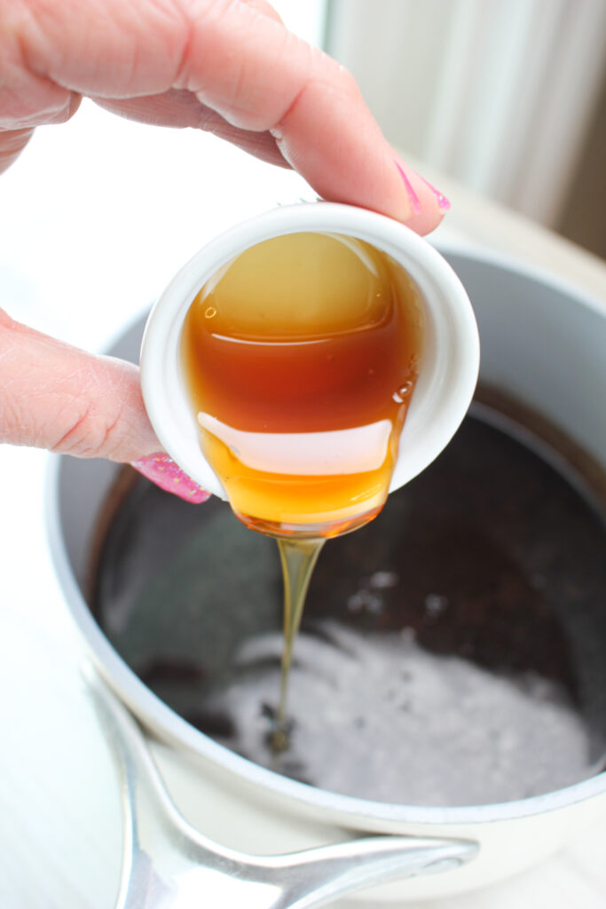 Adding honey to the saucepan of elderberry syrup.