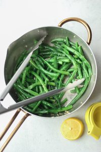 Fresh lemon juice has been squeezed over the cooked green beans in the pan.