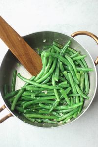 The green beans have been added to the pan of cooked garlic.
