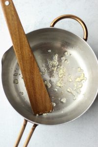 Minced garlic is cooking in a medium stainless steel pan.