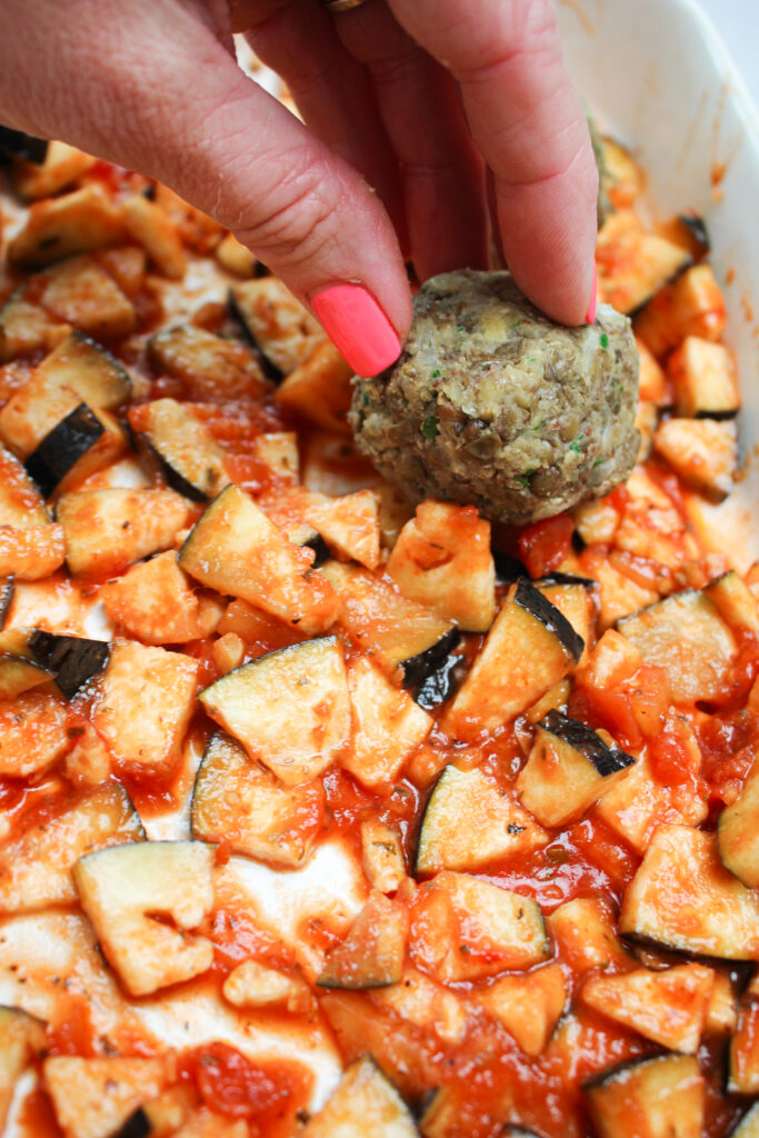 Adding the meatballs to the top of the eggplant and marinara. 