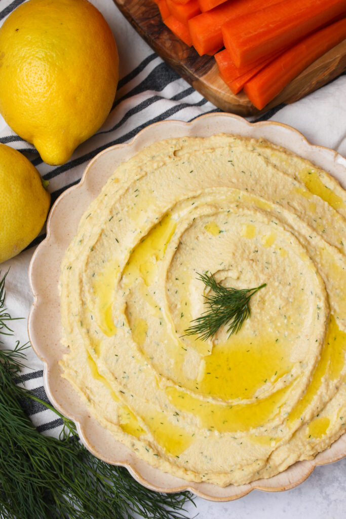 The lemon dill hummus is spread on a plate, drizzled with olive oil, and is ready to eat.