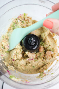 Using a spatula to scrape the bowl of the food processer.