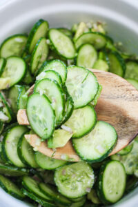 Tossing the salad with a large wooden spoon.