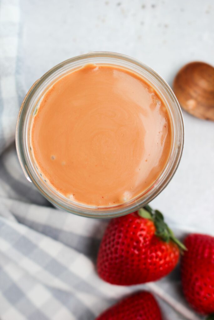 An upclose picture of the dressing in a mason jar with a few strawberries.