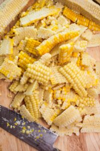 The corn kernals have just been cut off of the cobs and are on a cutting board.