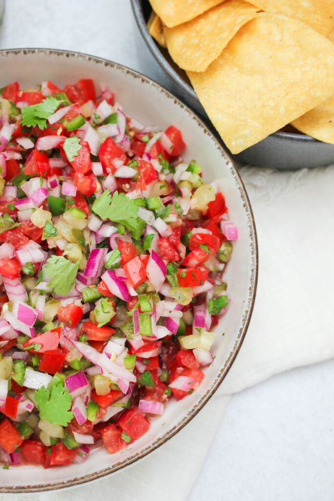 An upclose picture of the pickle de gallo in a bowl with another bowl of tortilla chips.