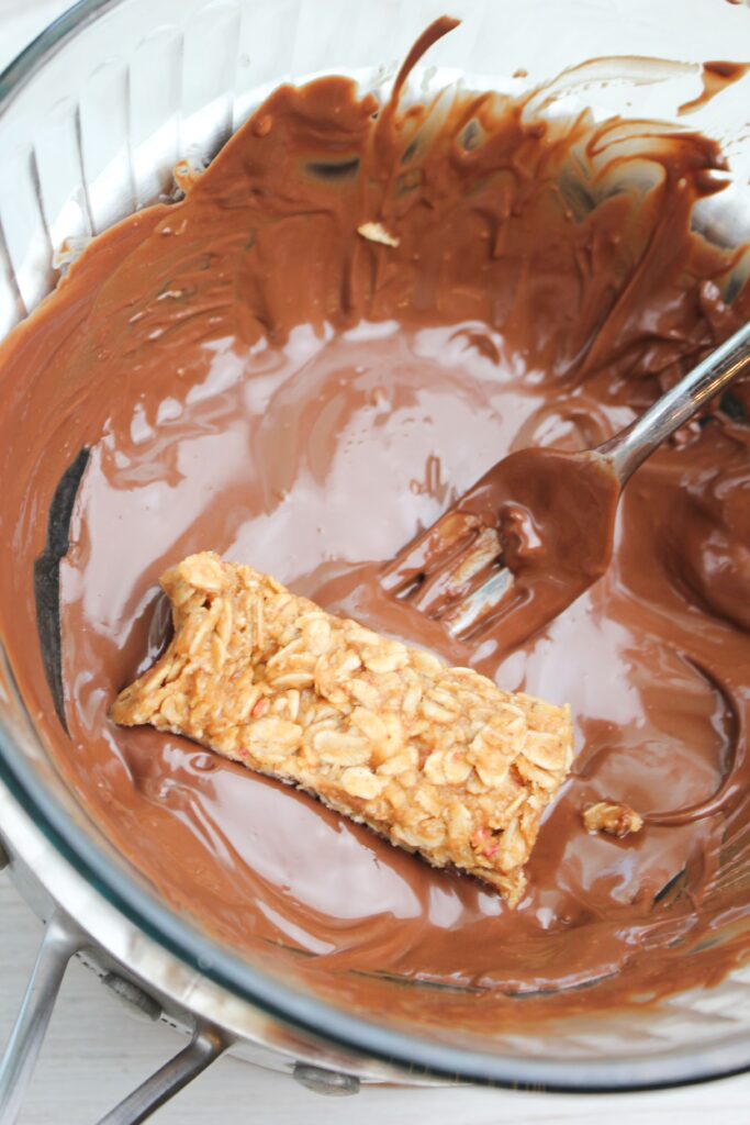 Dipping a granola bar into the bowl of melted chocolate. 