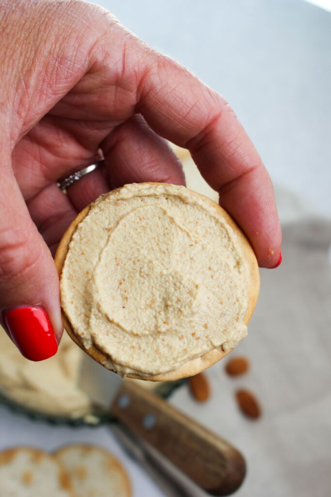 Holding a cracker with the almond dip spread on top.