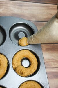 Pouring the batter into a donut mold with a piping bag.