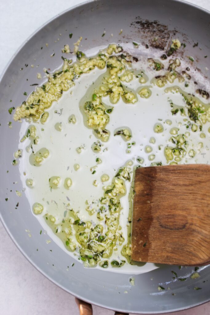 Cooking oil, garlic, and rosemary in a pan.