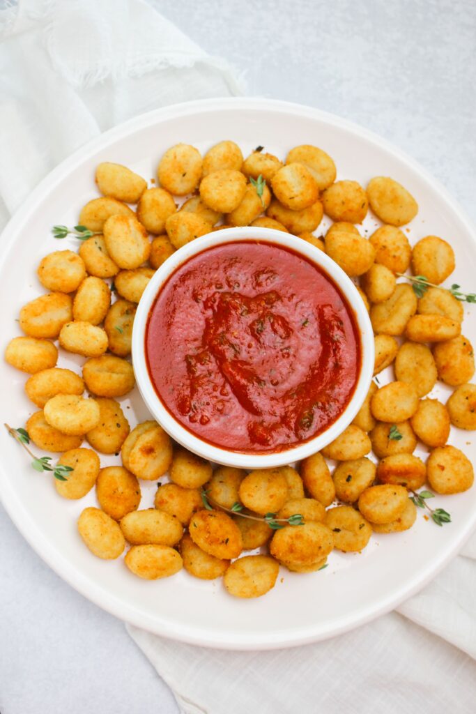 A platter of the air fried gnocchi with a small cup of marinara and is ready to be served.