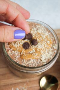 Adding the toppings to the mason jar of chocolate chia seed pudding.