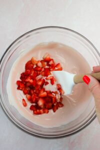 Folding in chopped strawberries into the yogurt mixture.