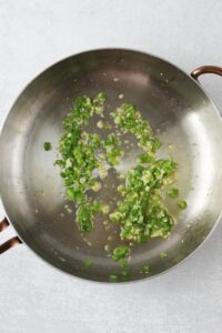 The olive oil, minced garlic, and minced jalapeno are frying in a pan.