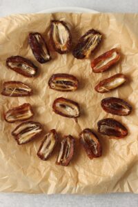 The dates are cut in half and placed on a parchment paper-lined plate.