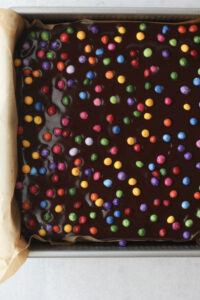 The ganache has been poured over the oat mixture and topped with the colored chocolate chips.