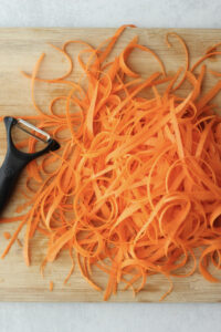 Shredding the carrots into ribbons on a cutting board.